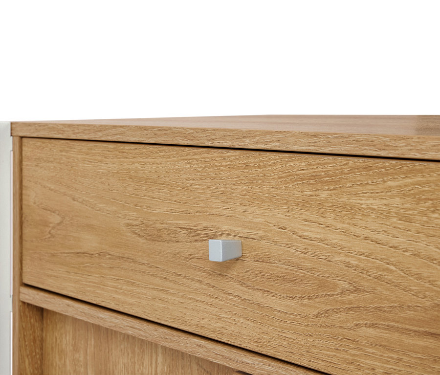 Detailní záběr na světle hnědou dřevěnou komodu se stříbrnou rukojetí.