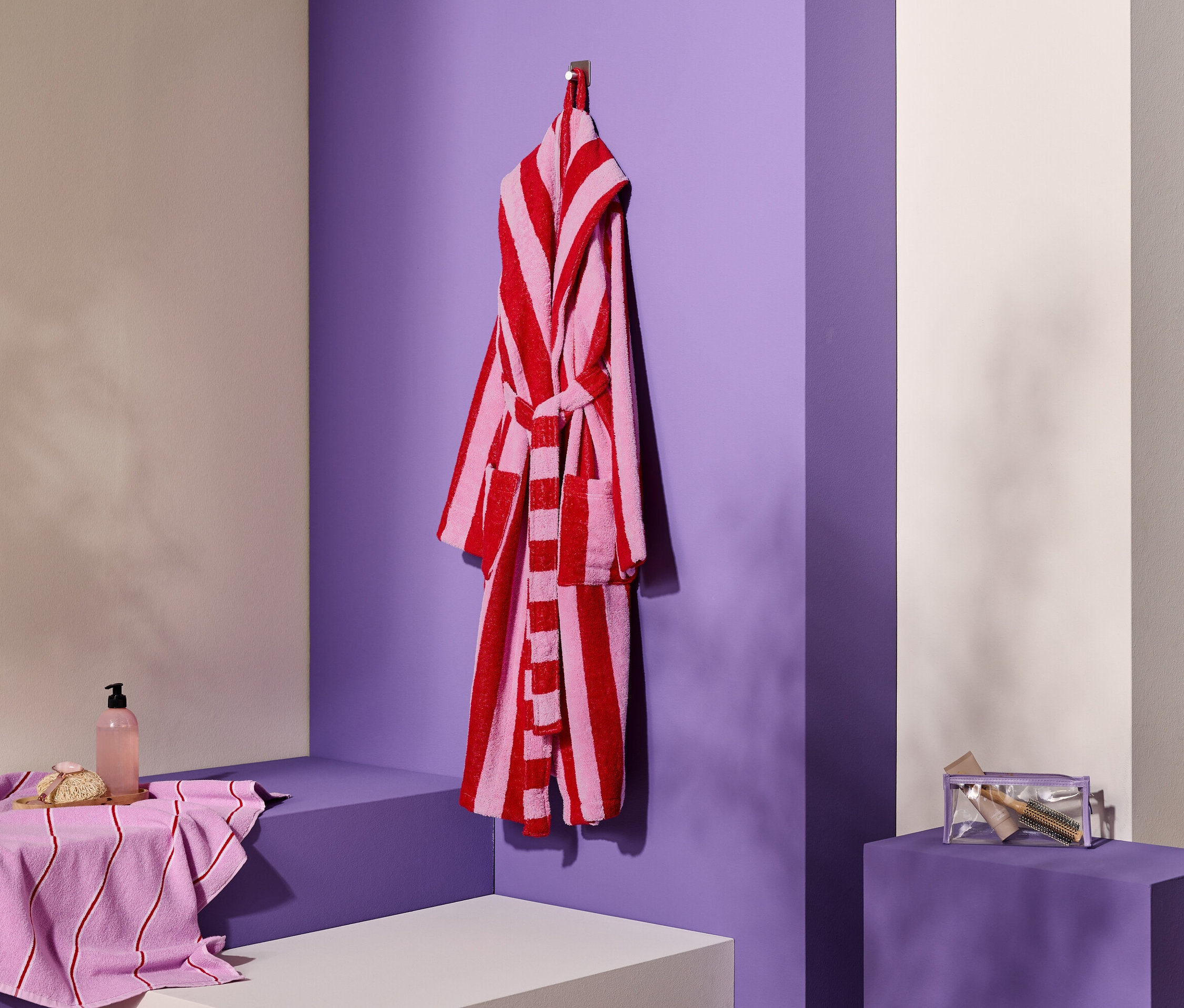 Pruhovaný župan visí na háčku vedle ručníku, mýdla a kosmetické taštičky.