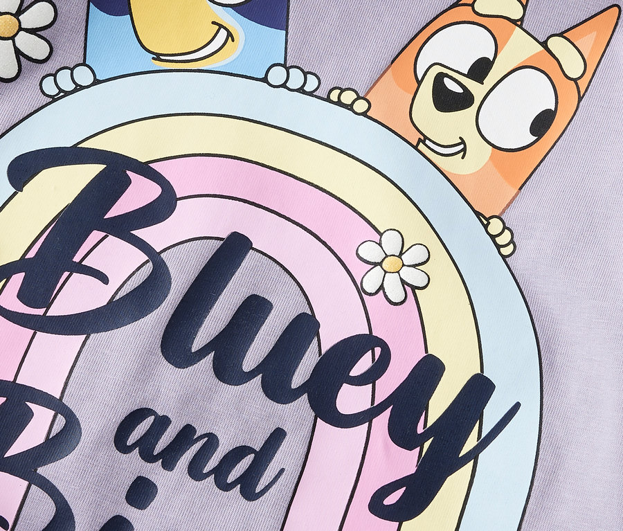 Detail fialové látky s kreslenými postavičkami Bluey a Bingo, které vykukují zpoza duhy, a také sedmikrásky.