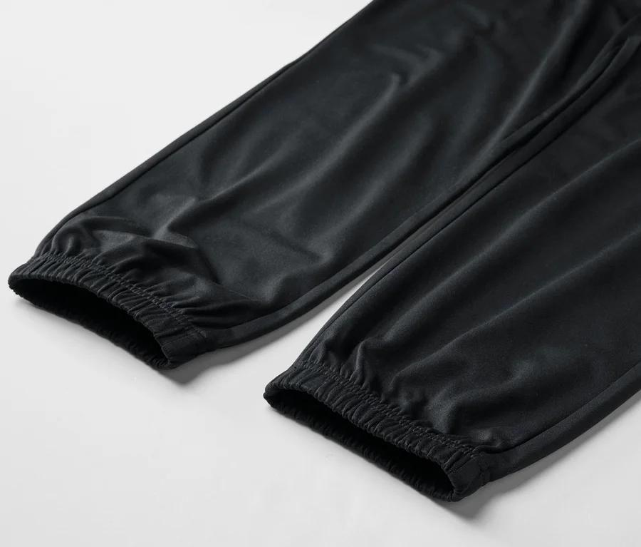 Detail dvou nohavic černých tepláků s elastickými manžetami na bílém pozadí.