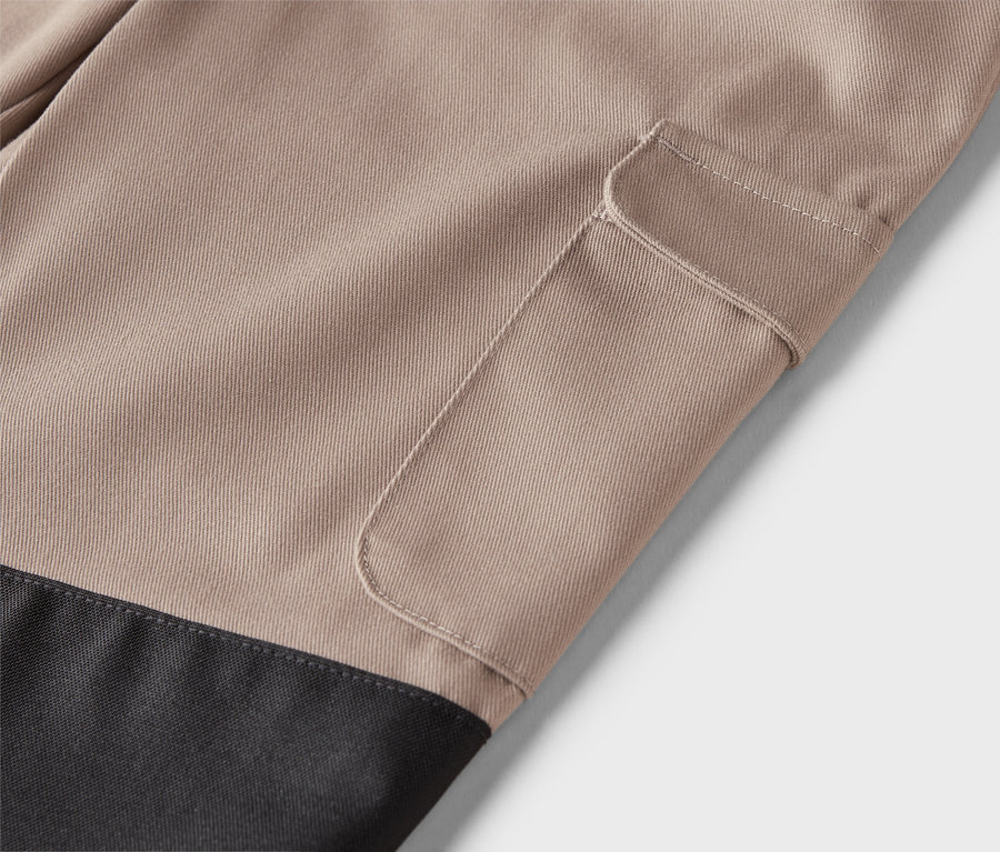 Detail béžových kalhot s našitou kapsou a černou spodní částí.