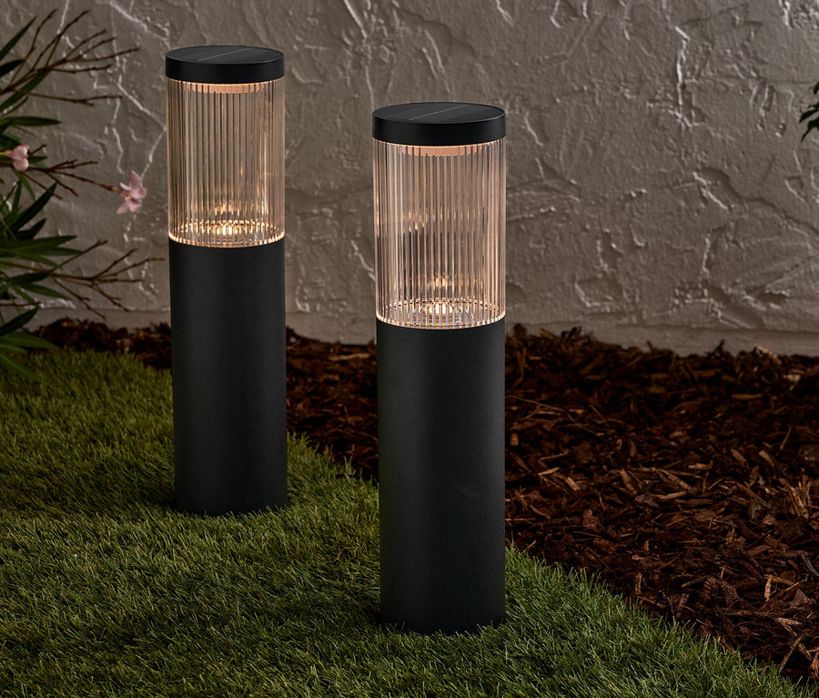 Dvě černé solární lampy stojí na trávníku před zdí.