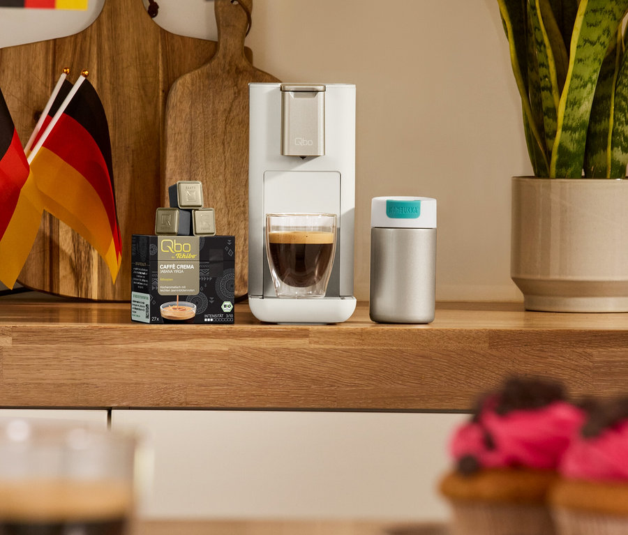 Kávovar Qbo ICONIC Light Gold, 2 sklenice Caffè Crema s dvojitými stěnami a Cestovní hrnek Kambukka, light gold na kuchyňské lince.