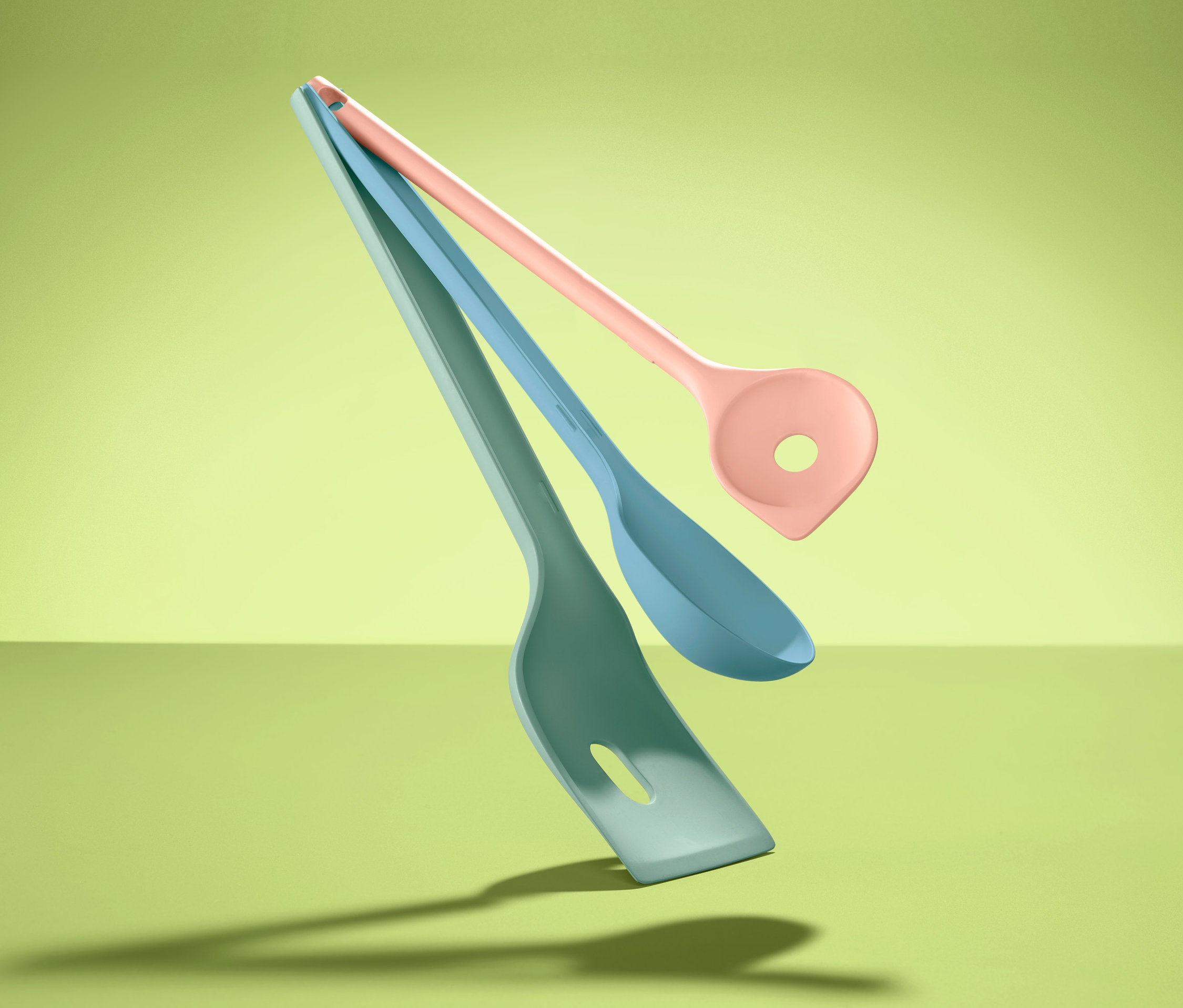 Tři barevné kuchyňské potřeby (obracečka, lžíce, naběračka) na zeleném pozadí.