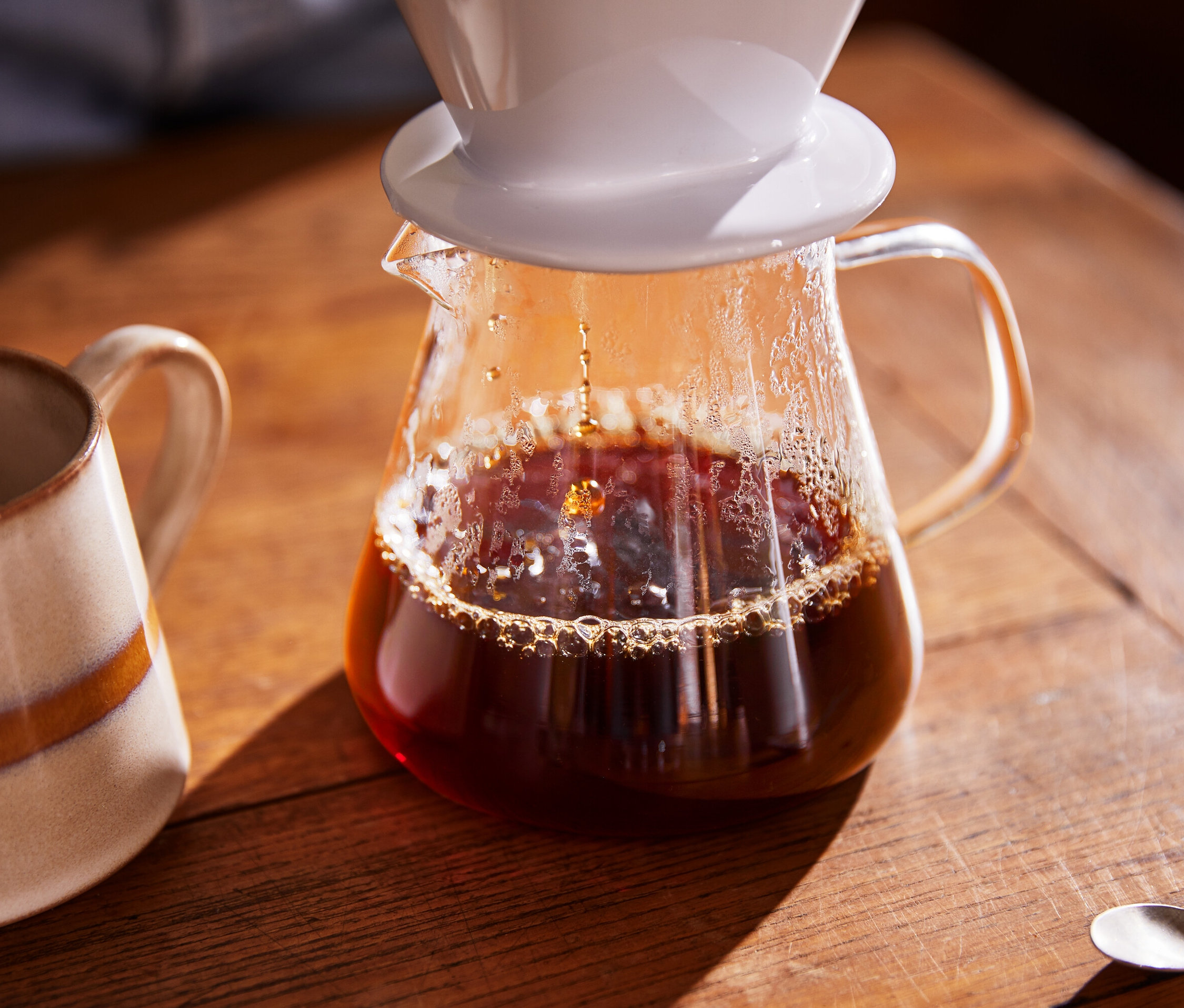 Káva se lije do skleněné konvice na kávu, vedle stojí hrnek.