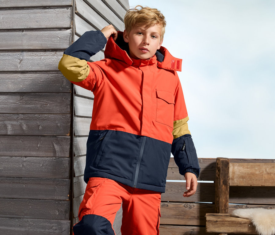 Chlapec v oranžovo-tmavě modré snowboardové bundě.