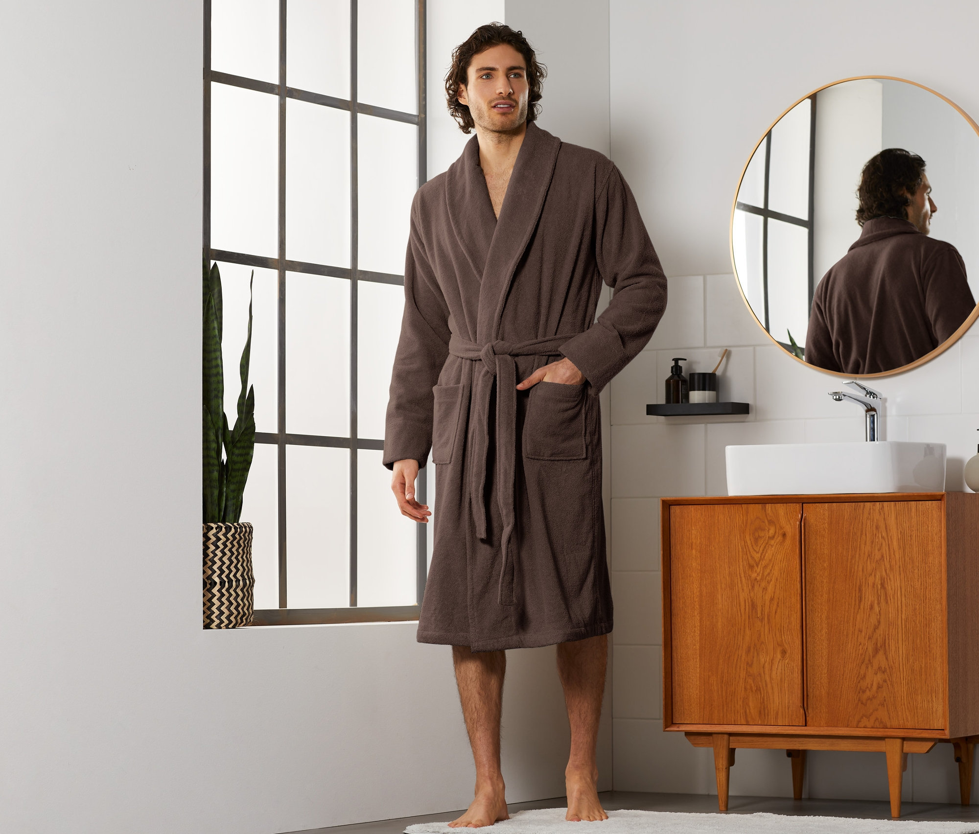 Muž stojí v koupelně a má na sobě hnědý župan.