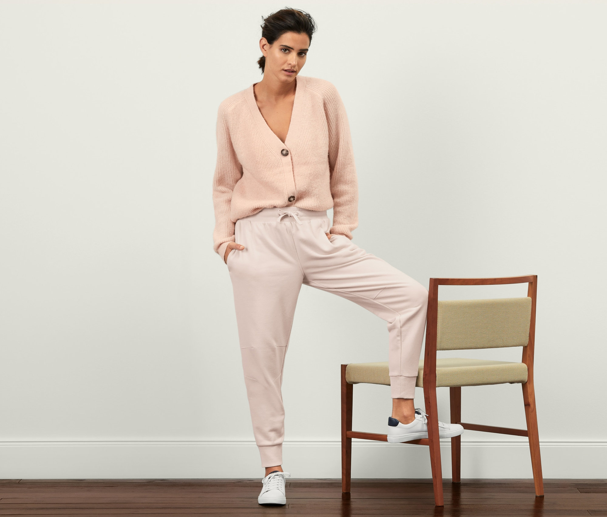 Žena pózuje s jednou nohou na židli a má na sobě tepláky.