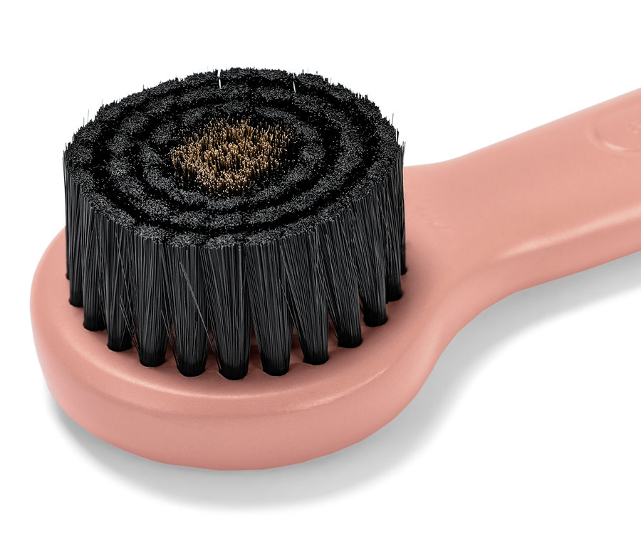 Detailní záběr obličejového masážního kartáče s měděnými štětinami s růžovou rukojetí.