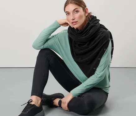 Žena sedí na podlaze a má na sobě černou oversize šálu 3 v 1.
