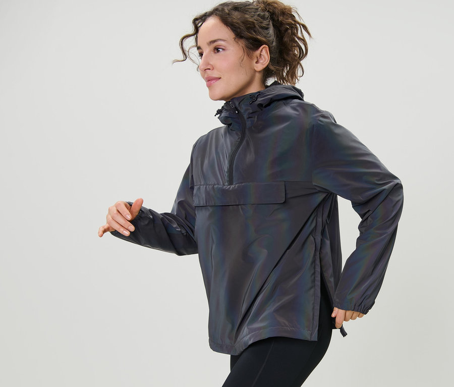 Žena v pohybu má na sobě duhovou reflexní větrovku a černé legíny.