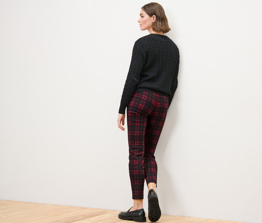 Žena stojí zády ke kameře a má na sobě kostkované strečové kalhoty, černý svetr a černé boty.