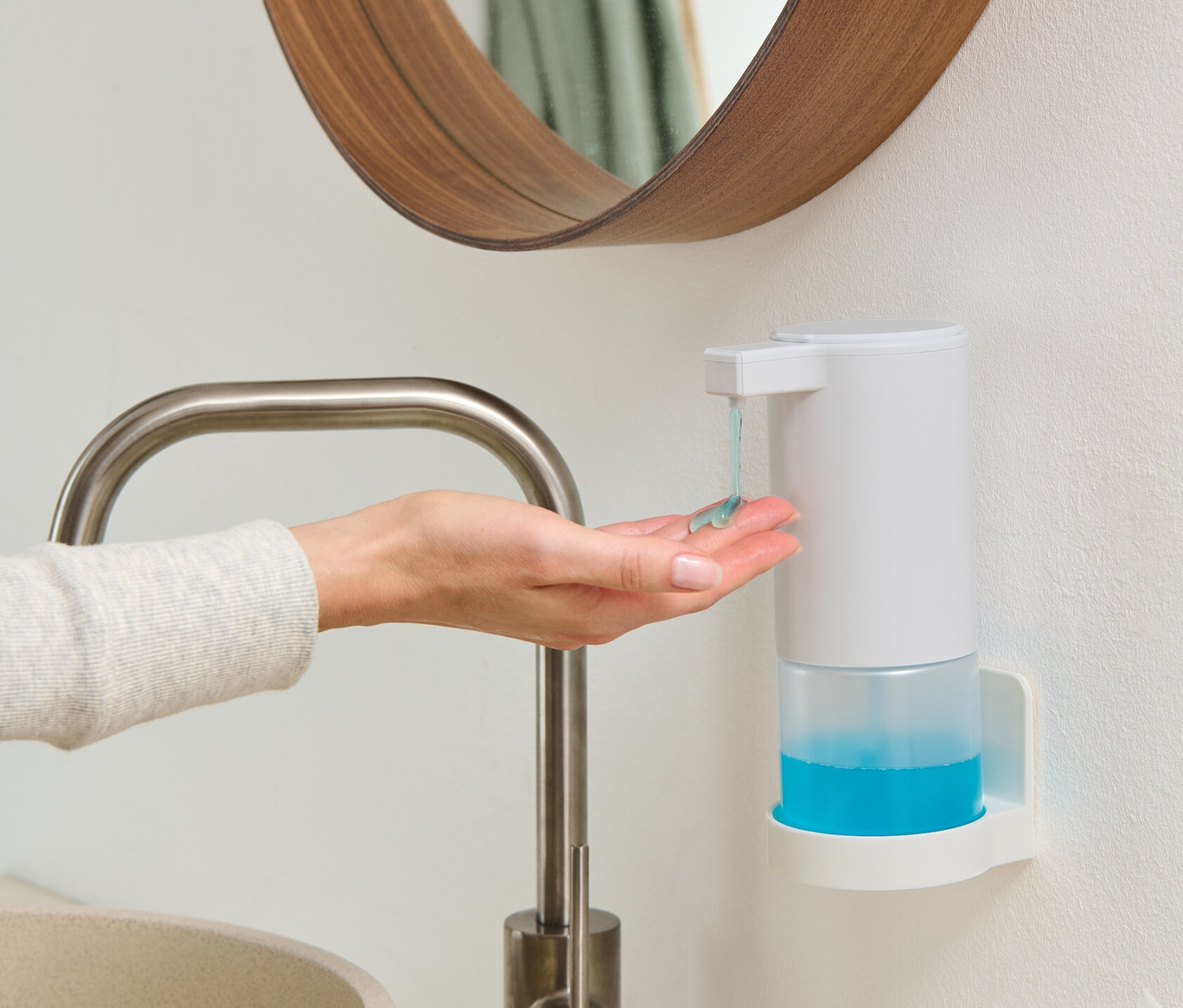 Žena si dává do dlaně mýdlo z bílého dávkovače mýdla se senzorem, který je namontovaný na zdi.