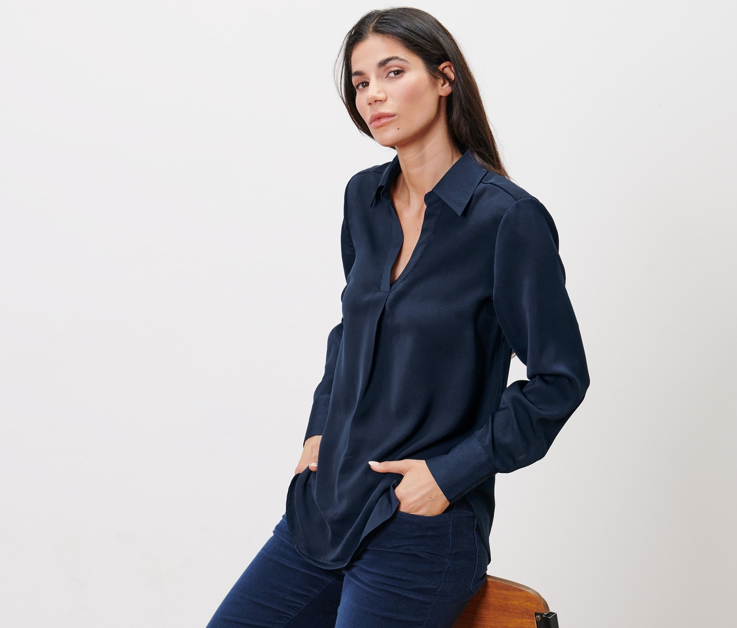 Žena sedí na židli a má na sobě saténovou halenku.