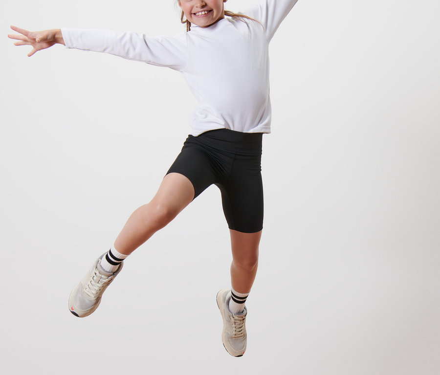 Dívka skáče na dřevěném podstavci a má na sobě černé sportovní šortky a bílé tričko s dlouhým rukávem. Na sobě má Dětské sportovní šortky 2 ks.