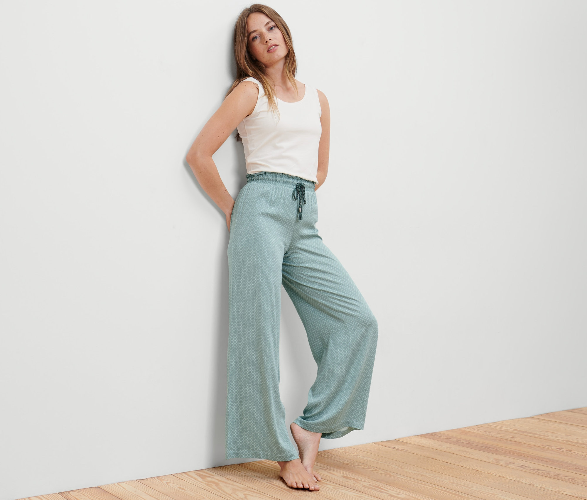 Žena opřená o stěnu pózuje v petrolejových pohodlných kalhotách.