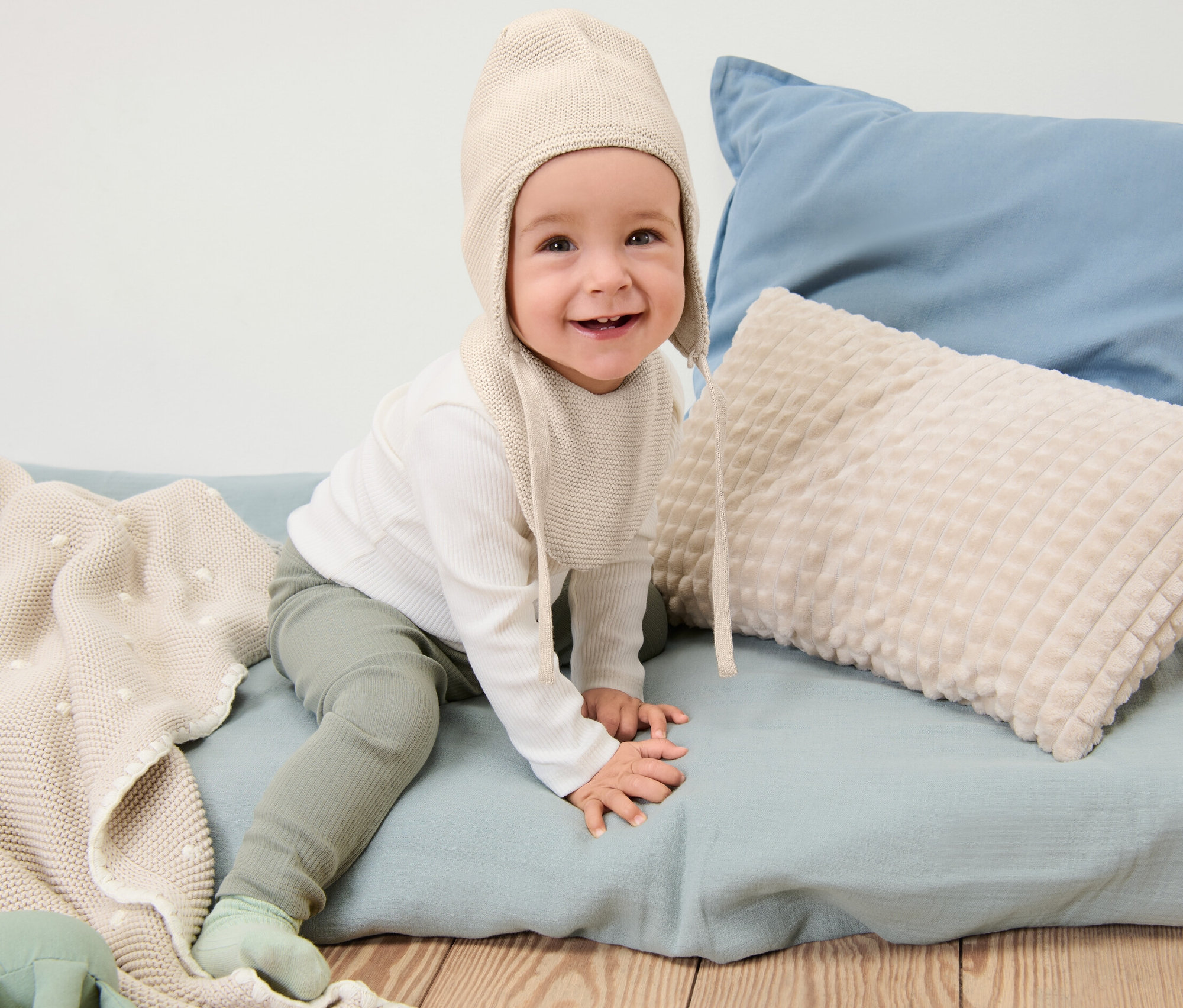 Usmívající se dítě sedí a má na sobě pletenou čepici a šálu pro miminka.