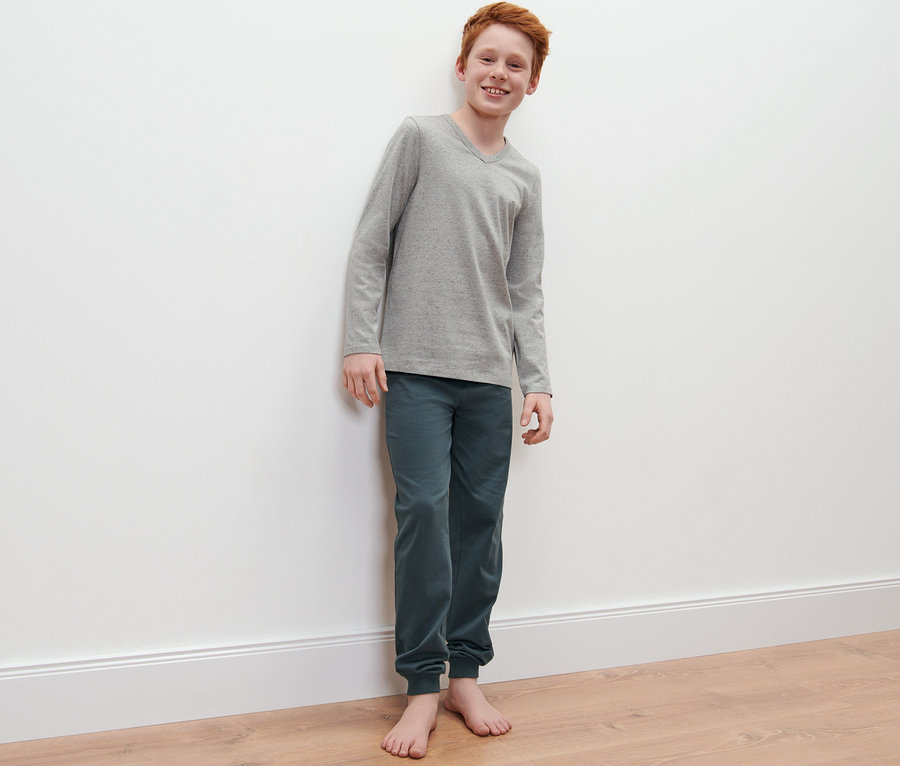 Chlapec pózuje v dětském pyžamu, 2 ks, šedé tričko s dlouhým rukávem a zelenomodré kalhoty.