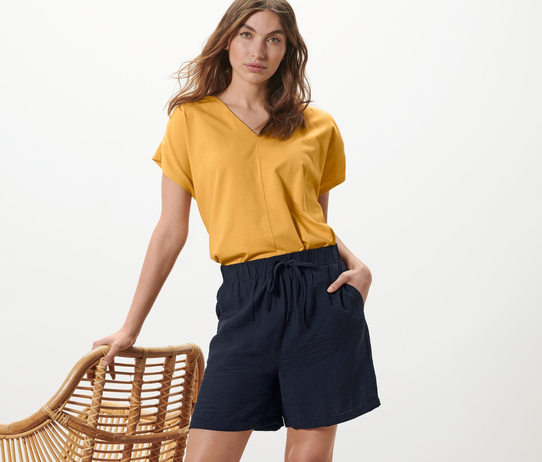 Žena pózuje v žlutém topu a tmavě modrých šortkách.