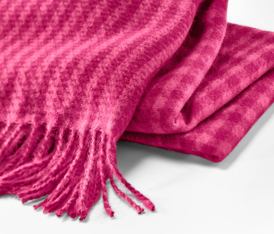 Detail tkané šály s třásněmi malinové barvy.
