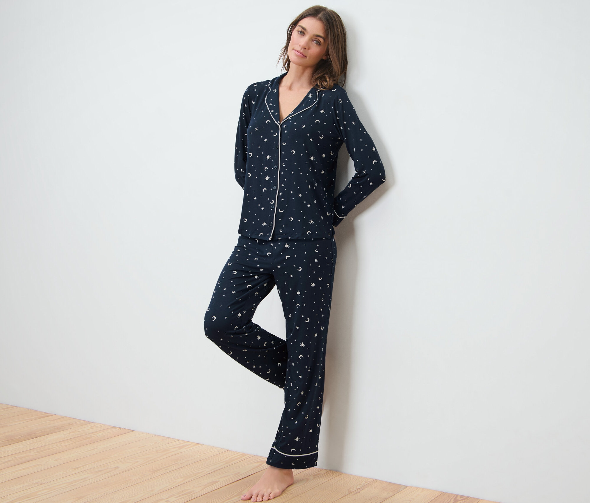 Žena opřená o bílou zeď má na sobě tmavě modré pyžamo s hvězdnou oblohou.