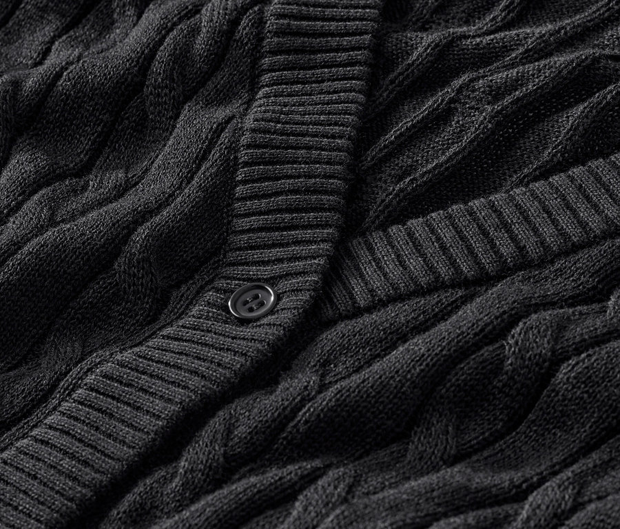 Detail černého kardiganu z jemného úpletu s copánkovým vzorem.