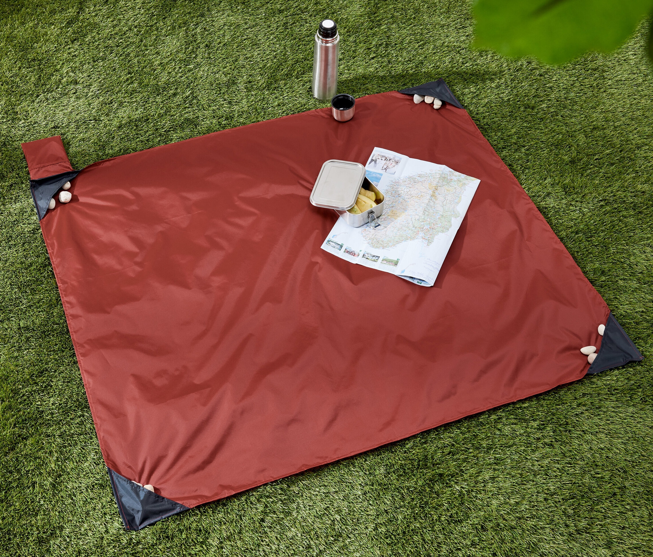 Na trávě leží minideka na piknik, na níž je mapa a svačina. Vedle deky je termoska s hrnkem.