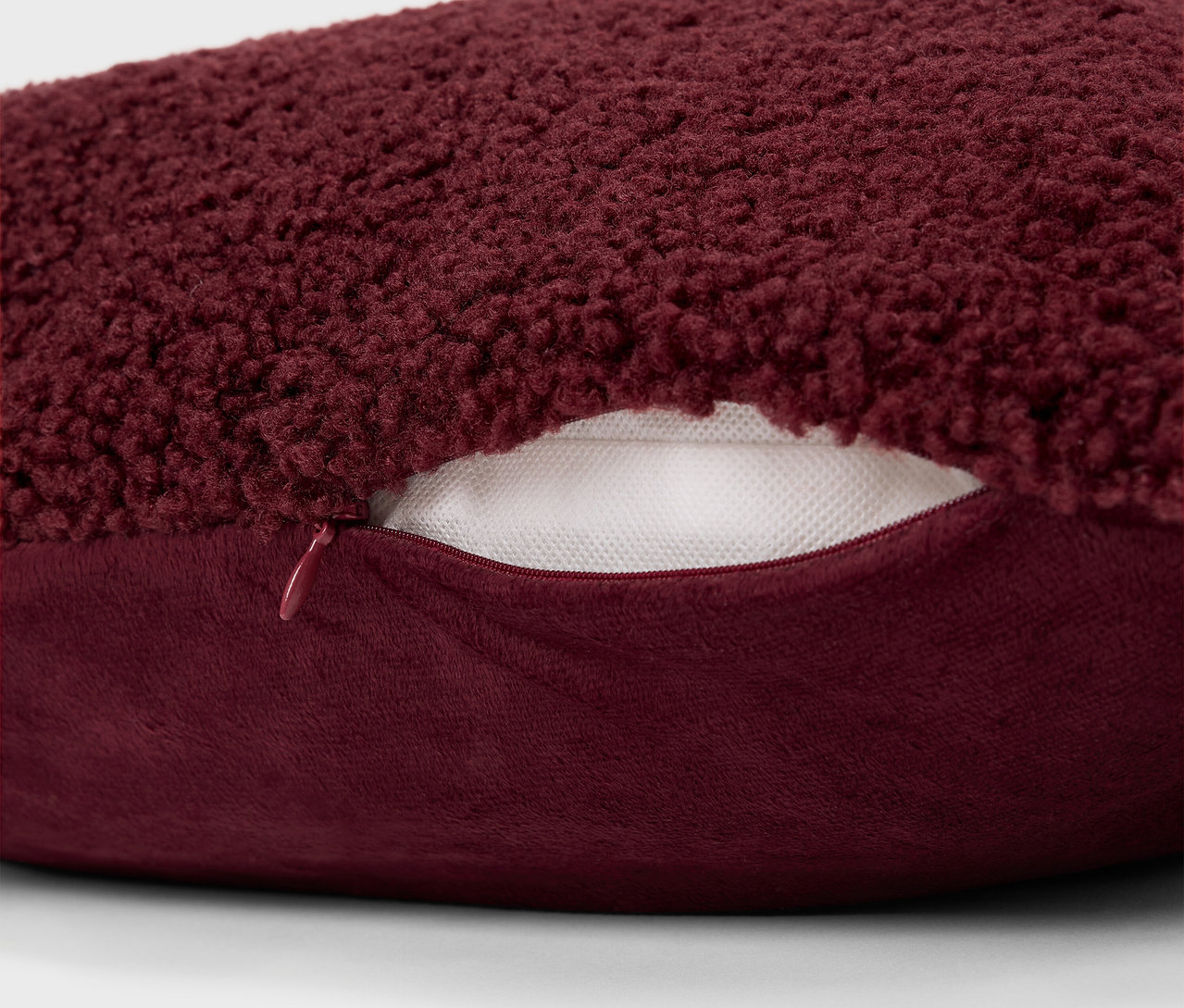 Detail bordó chlupatého polštáře se zipem.