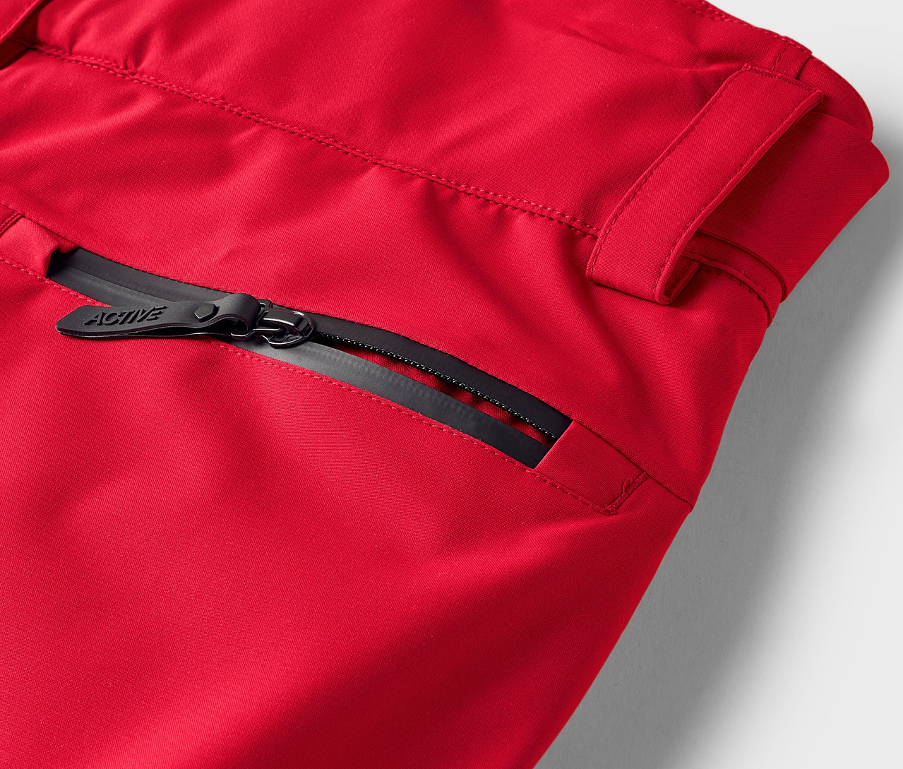 Detail červených kalhot s černým zipem na kapse.