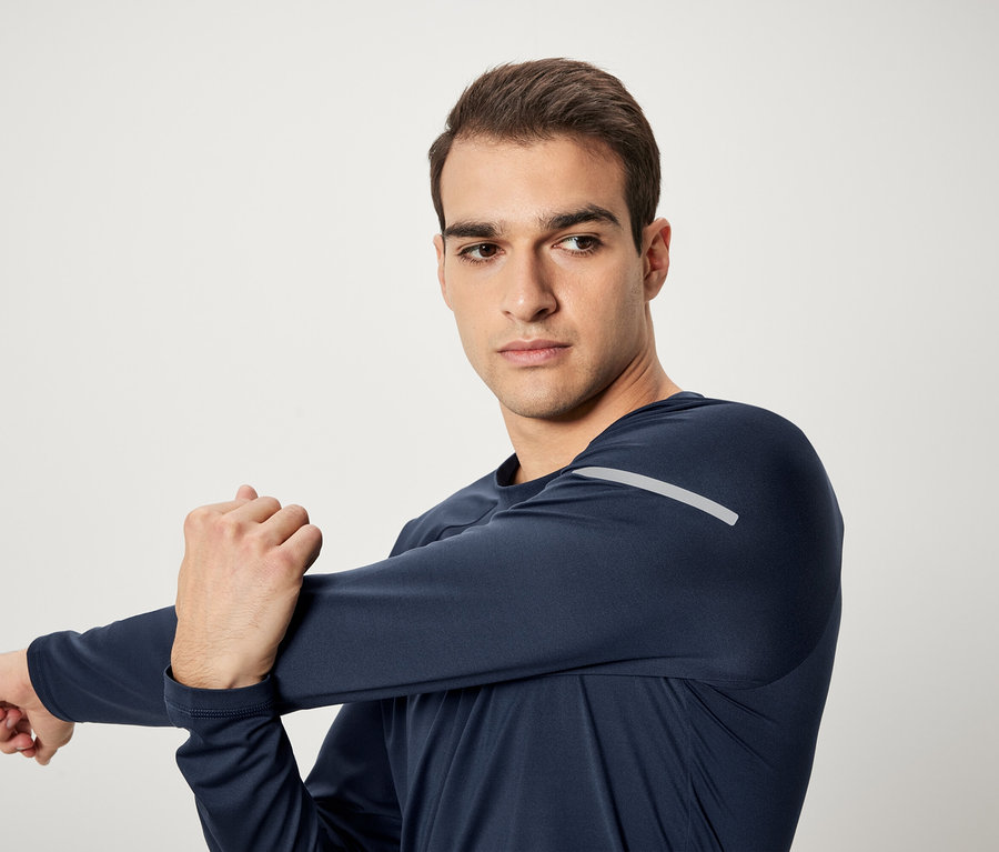 Muž protahuje paži v tmavě modrém sportovním tričku s dlouhým rukávem.