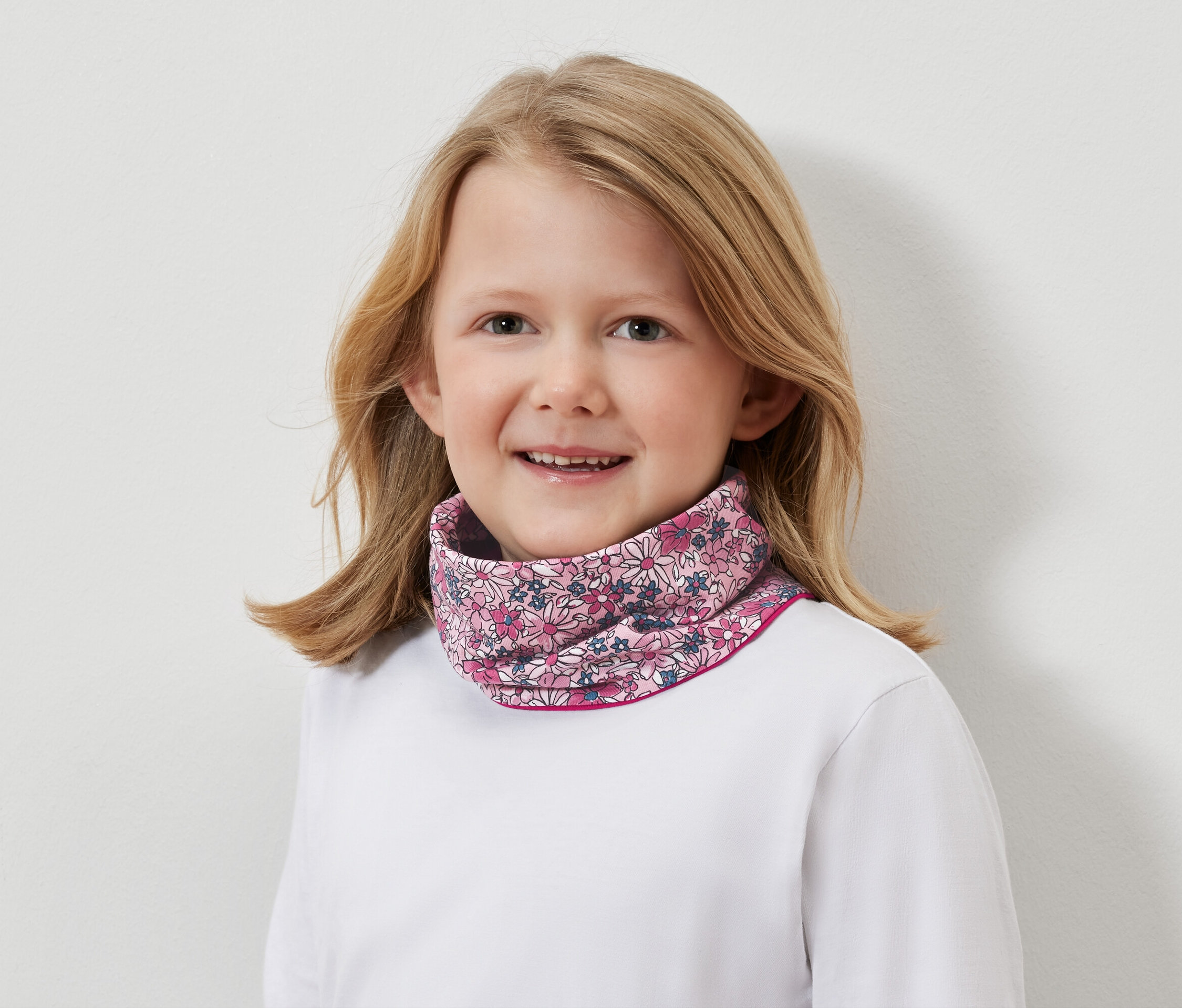 Portrét usmívající se blondýny s květinovým nákrčníkem.