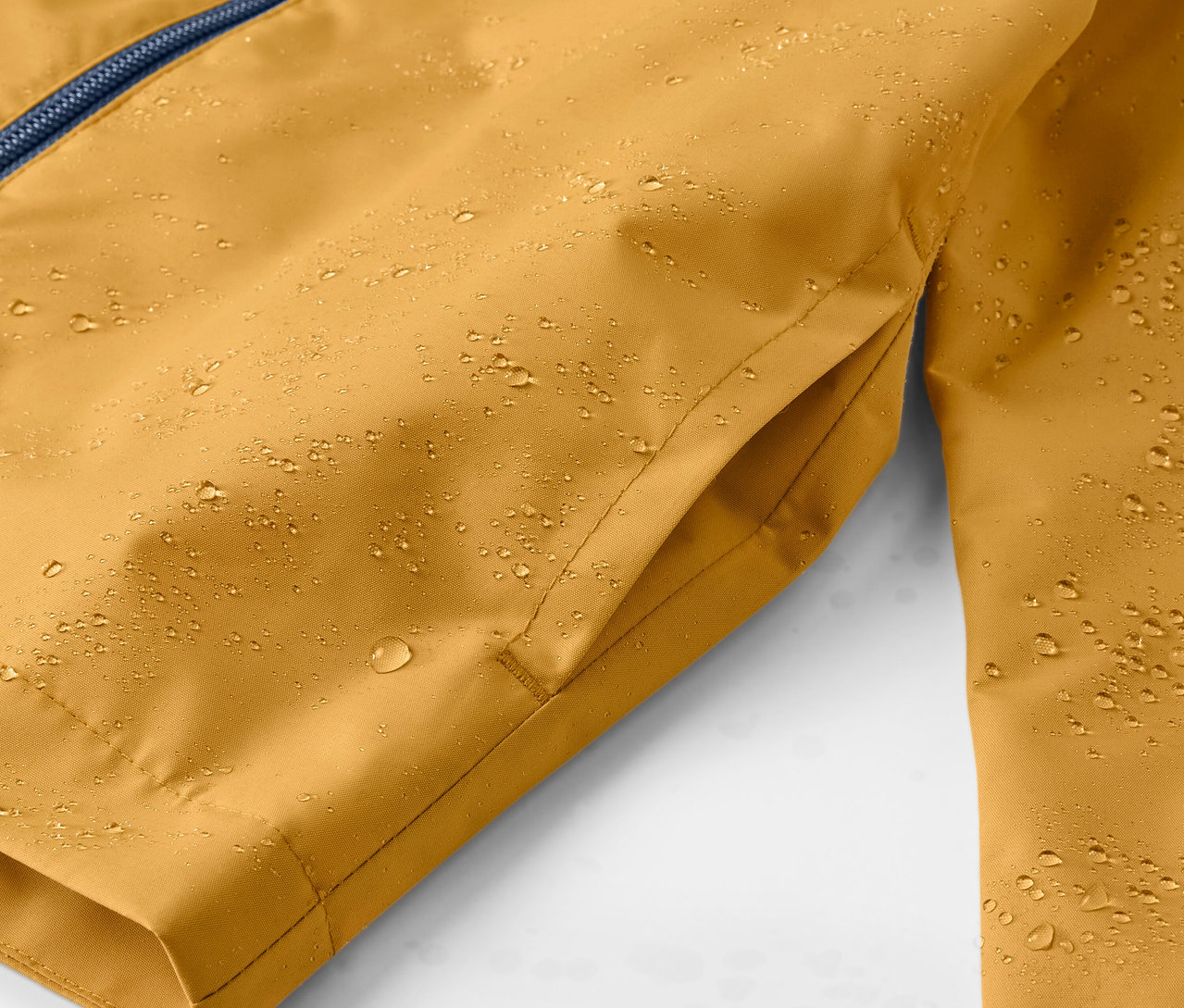 Detail žluté dětské bundy do deště s kapkami vody.