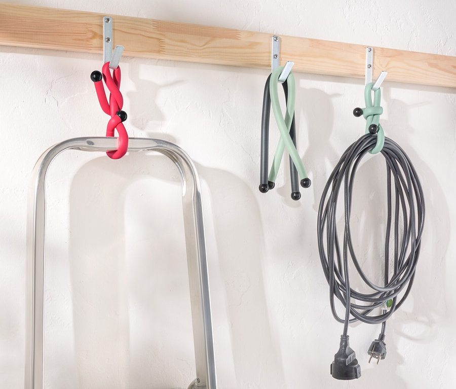 Žebřík stojí pod dřevěnou lištou s háčky, na kterých visí Power Kabelbinder v červené, zelené a černé barvě.