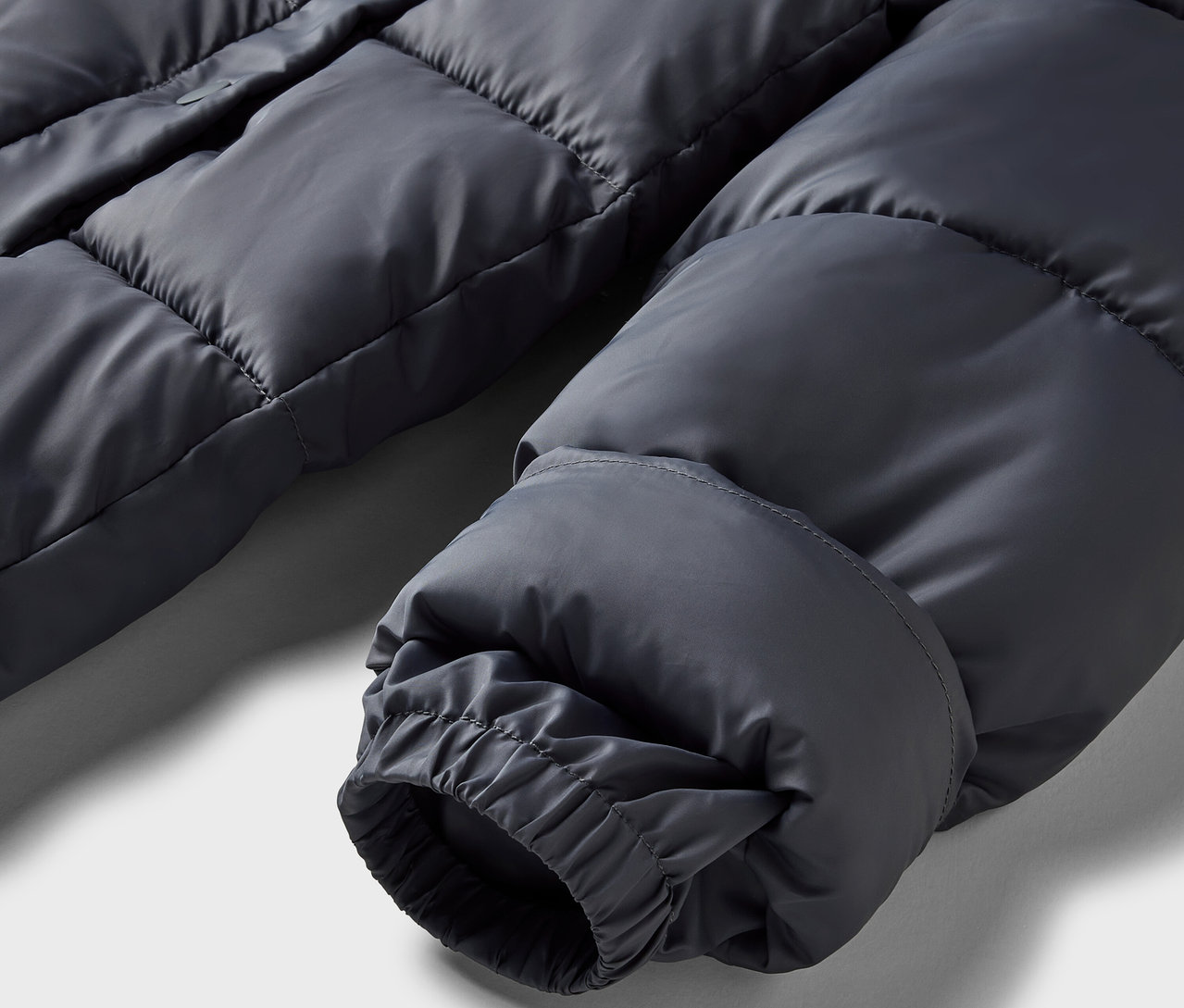 Detail šedé péřové bundy s elastickou manžetou.