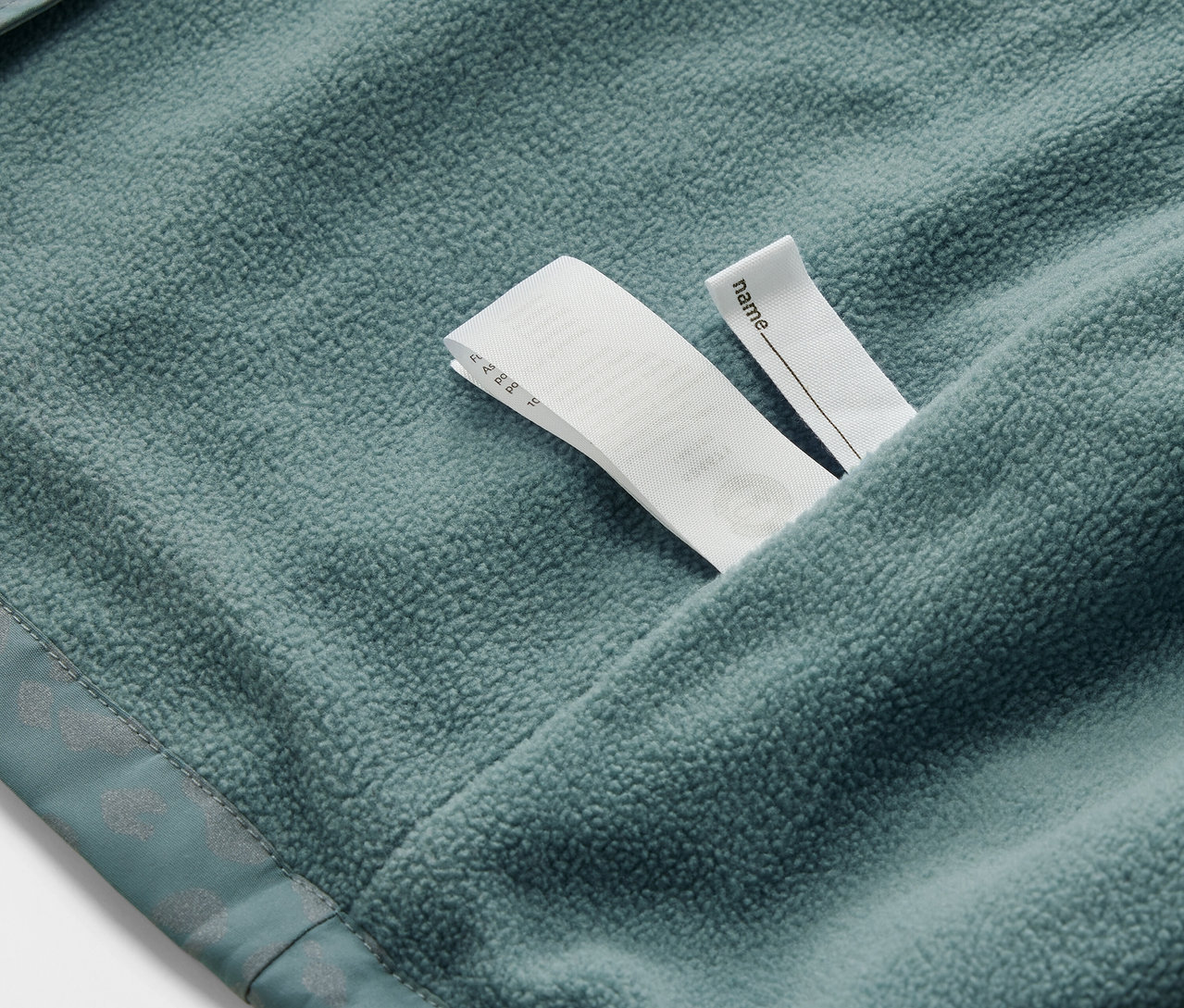 Detail dětské termo bundy do deště s reflexními prvky a štítkem na jméno.