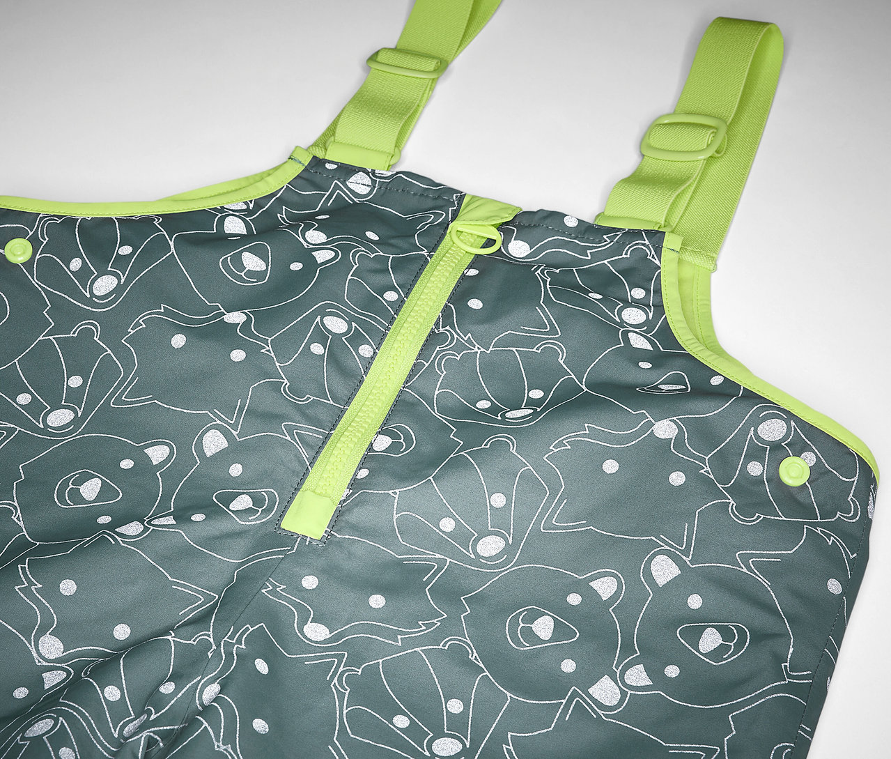 Detail dětských termo kalhot do deště s reflexními prvky, šedé s potiskem medvědů a lišek a žlutými popruhy.