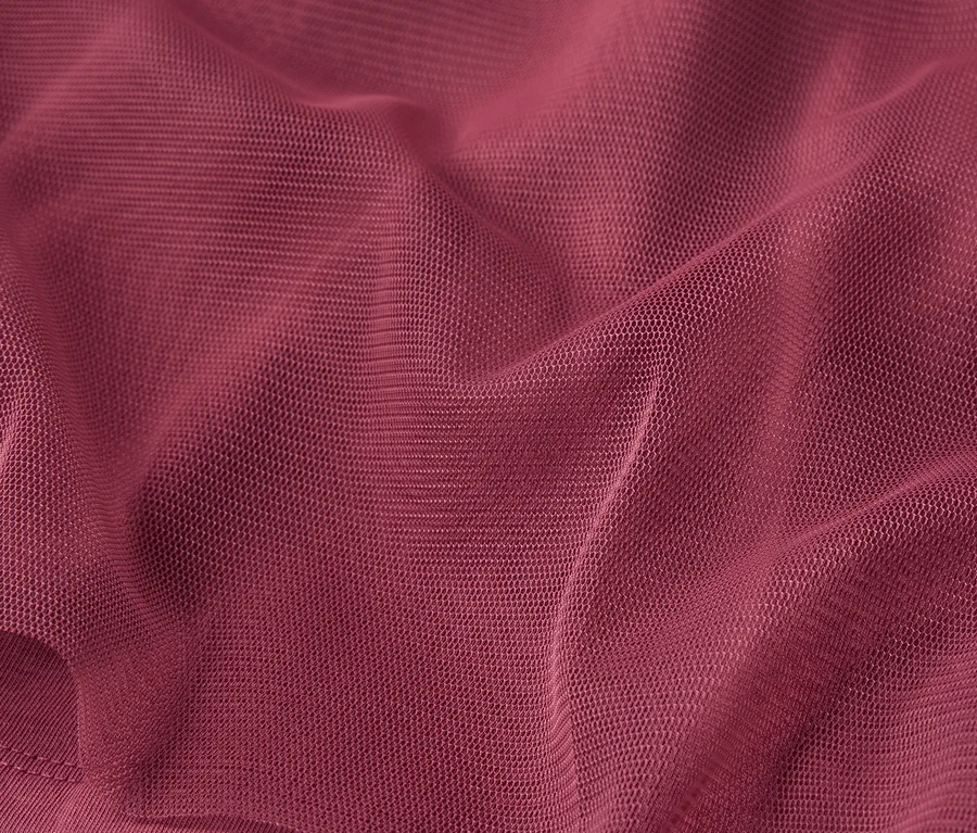 Detailní záběr na vínově červenou látku s jemnou texturou a záhyby.