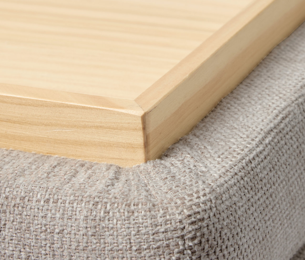 Detail dřevěného podnosu na šedém pufu.