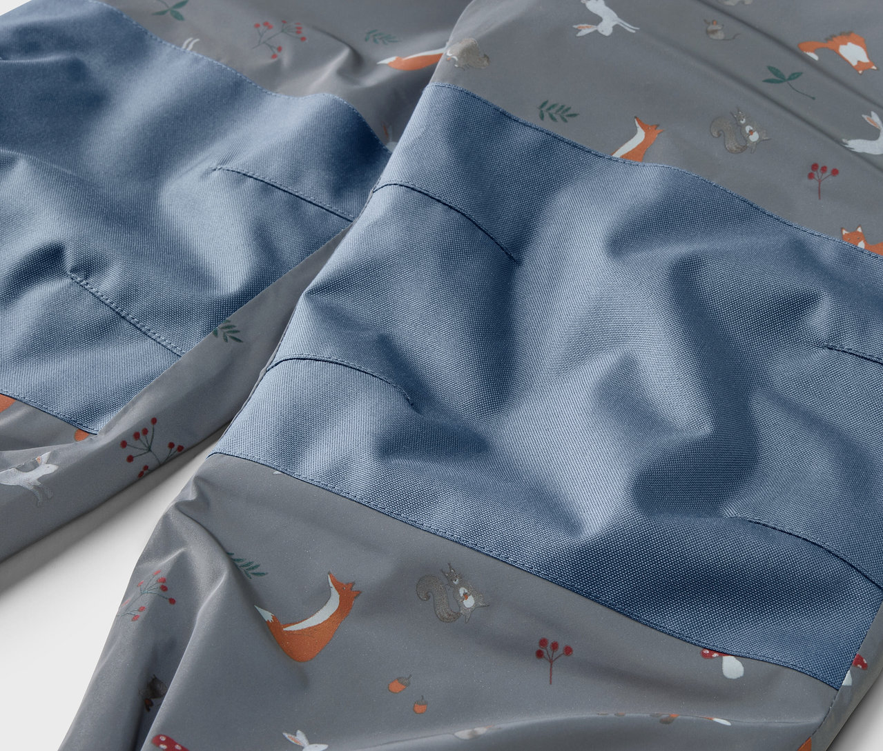 Detail dětských termo kalhot do deště s reflexními prvky a potiskem zvířat.