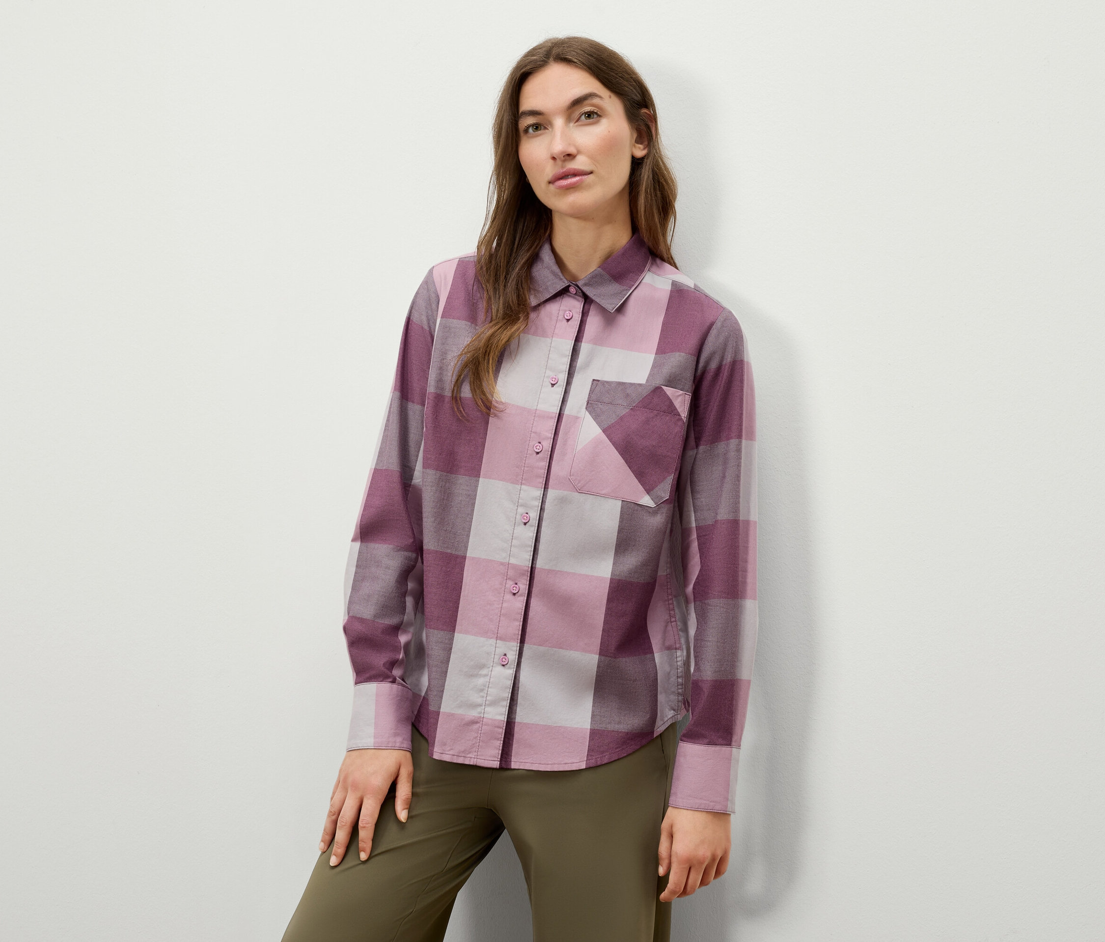 Žena pózuje v kostkované košili s dlouhým rukávem a olivově zelených kalhotách.