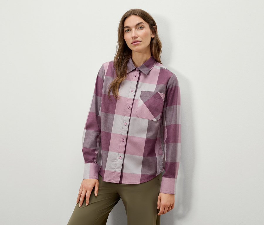 Žena pózuje v kostkované košili s dlouhým rukávem a olivově zelených kalhotách.