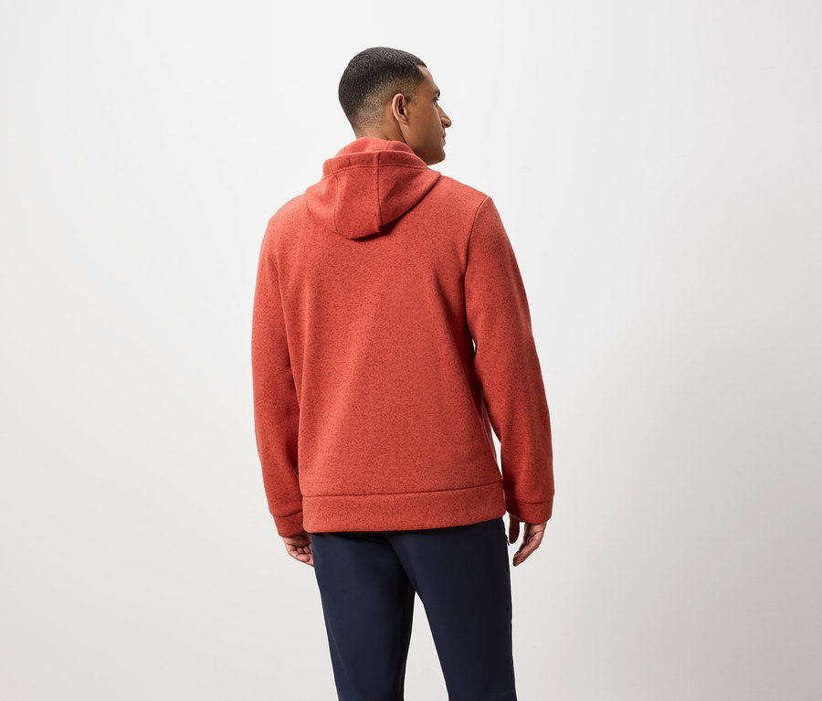 Muž zády k fotoaparátu má na sobě oranžovou mikinu s kapucí a tmavě modré kalhoty.