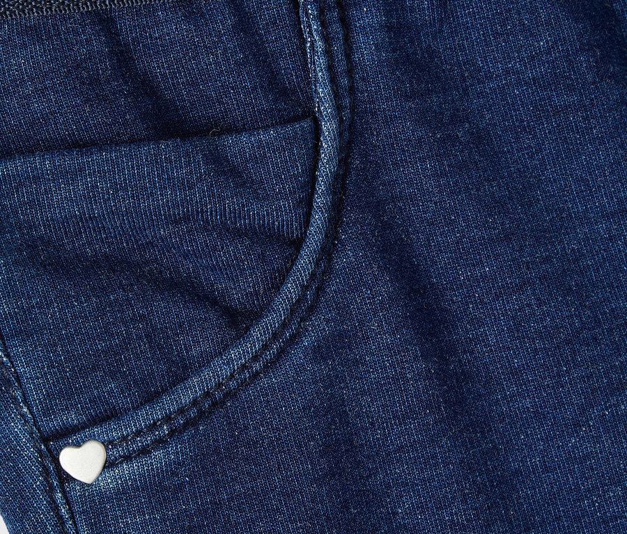 Detailní záběr na modré džínové kalhoty s malou kapsou a knoflíkem ve tvaru srdce.