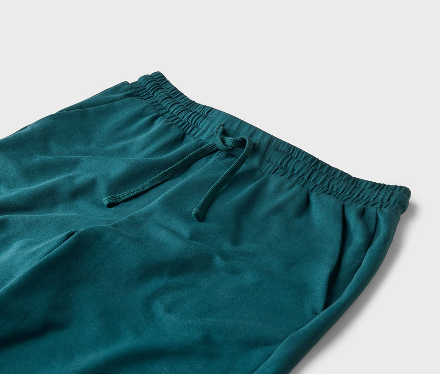 Detailní záběr na tyrkysové tepláky se stahovací šňůrkou a elastickým pasem na bílém pozadí.