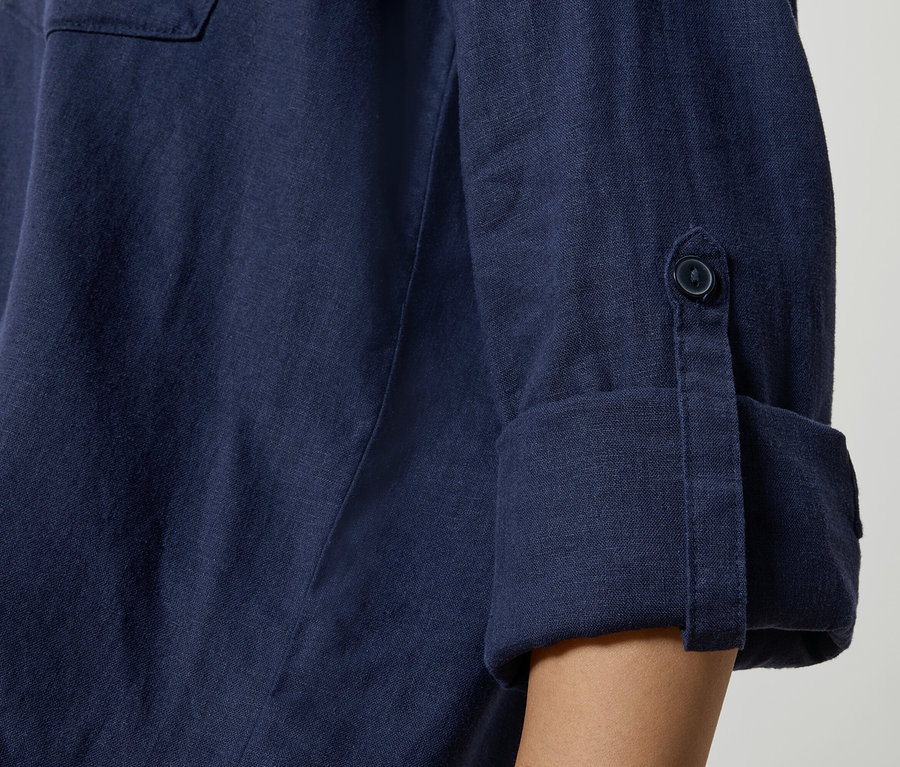 Detailní záběr na tmavě modrou lněnou košili s ohrnutými rukávy a detaily knoflíků.