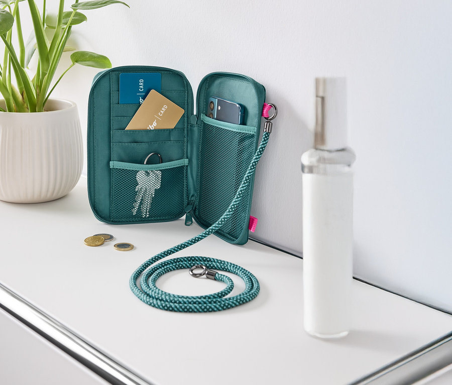 Otevřená zelená peněženka leží na bílém stole, vyplněná kartami, klíči a mobilním telefonem.