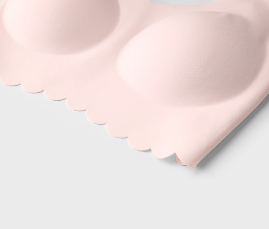 Detailní záběr světle růžové podprsenky se zvlněným lemem na bílém pozadí.