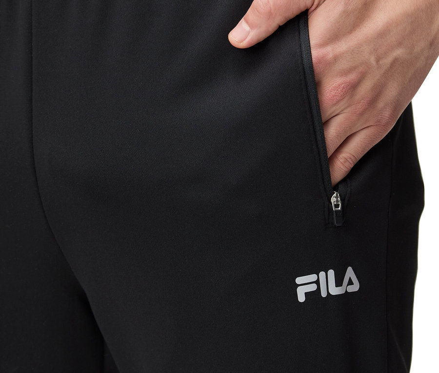 Muž si vkládá ruku do kapsy černých tepláků FILA.