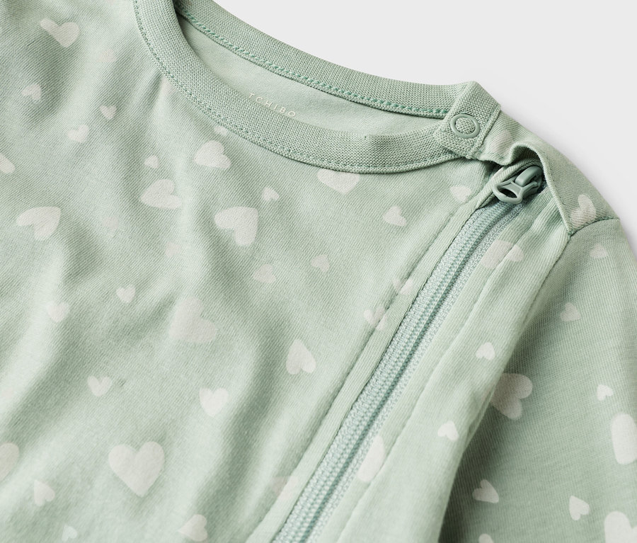 Detailní záběr světle zeleného dětského overalu s bílým vzorem srdce a zipem.