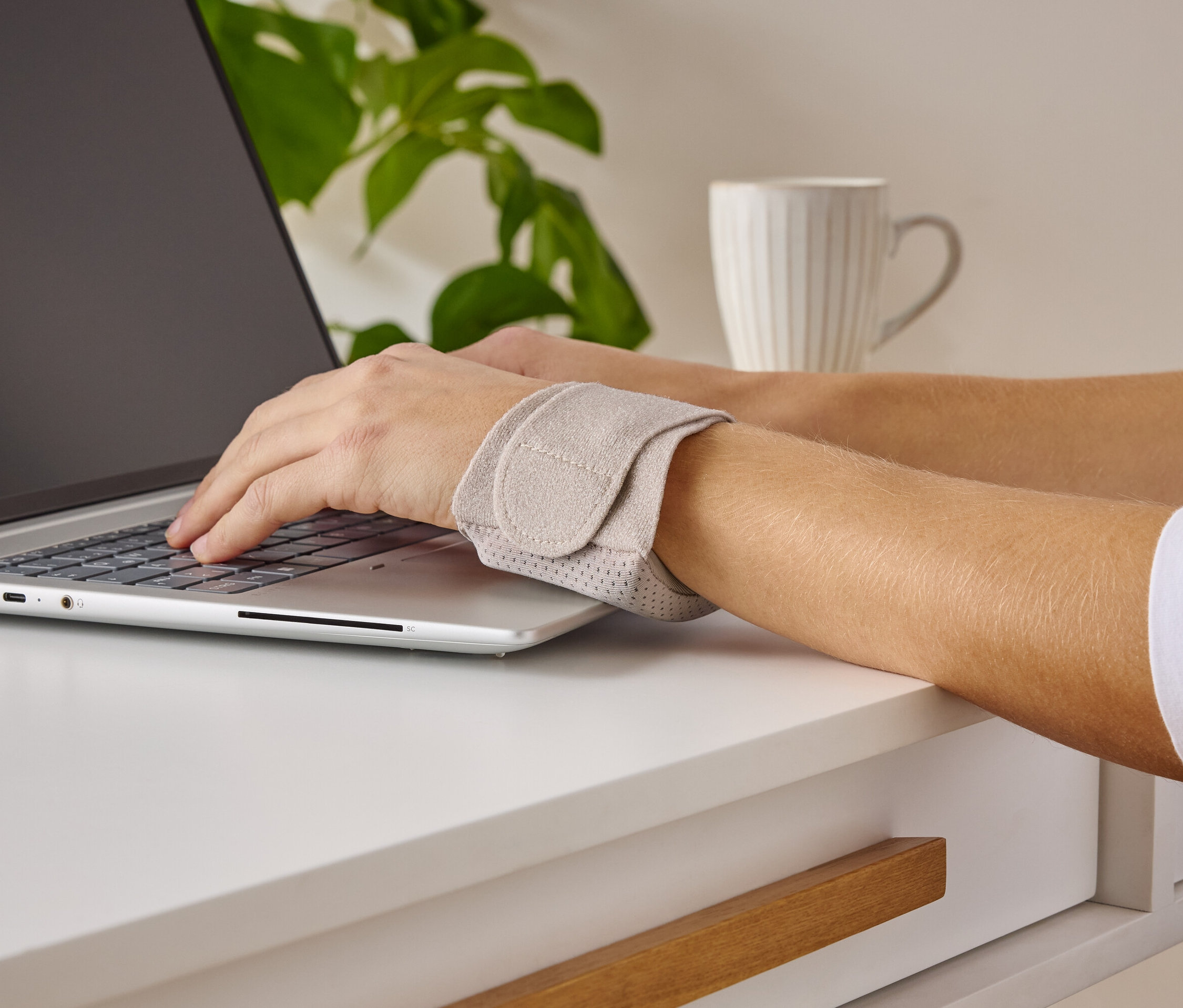 Osoba píše na notebooku a nosí podporu zápěstí.